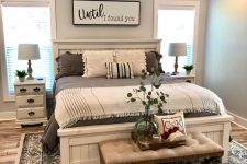 a blue farmhouse bedroom with a whitewashed bed, an upholstered bench, whitewashed nightstands, printed bedding and lights