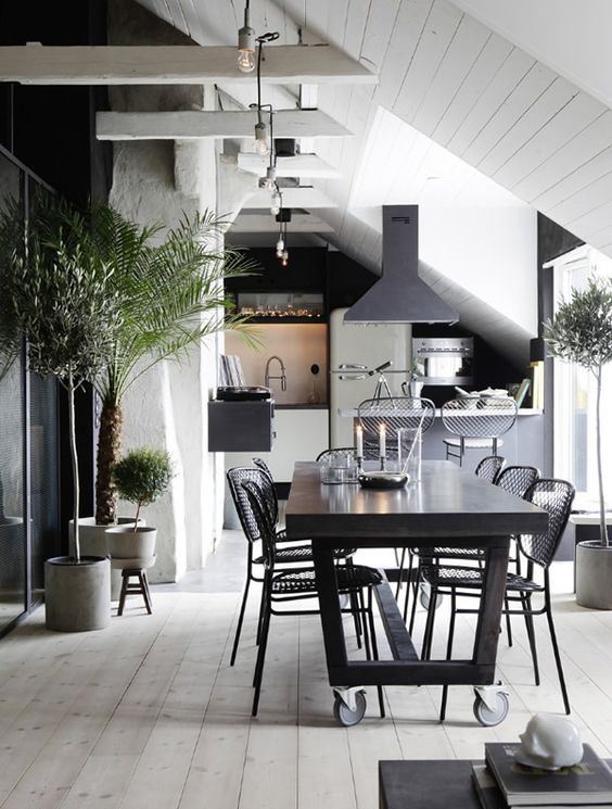 a bold kitchen and dining room, wiht white wood and plaster walls, a whitewashed floor and black furniture and pendant lamps