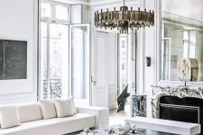a breathtaking French chic living room with a marble fireplace, a stone slab table, white and creamy seating furniture and a statement chandelier
