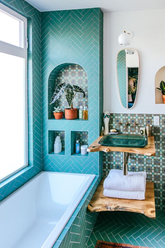 a bungalow bathroom with turquoise chevron tiles, beautiful Moroccan ones on the wall, a turquoise glass sink and a catchy mirror