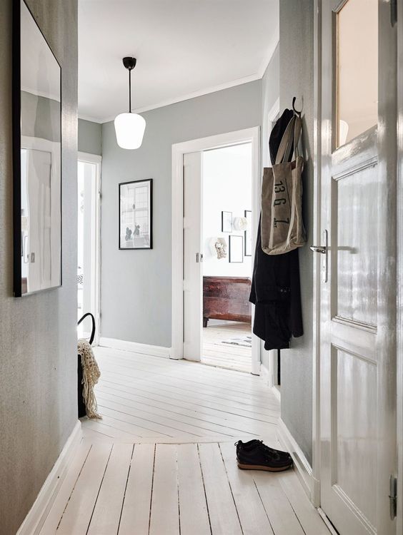 a casual entryway with light grey walls, a whitewashed wooden floor and gorgeous artworks to make the space cooler