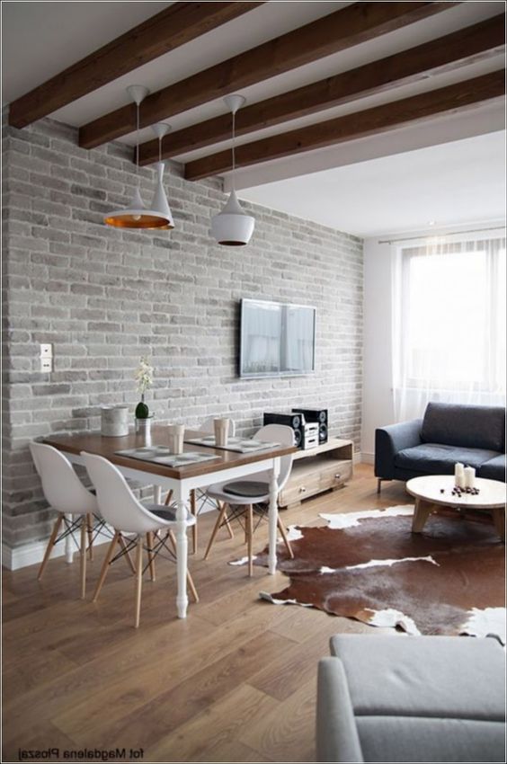 a contemporary space with a living room and a dining zone, a whitewashed brick wall, wooden beams and chic furniture