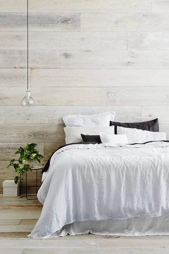 a contemporary yet a bit rustic bedroom with a whitewashed wood headboard wall and a floor, a comfy bed, a pendant lamp and a potted plant