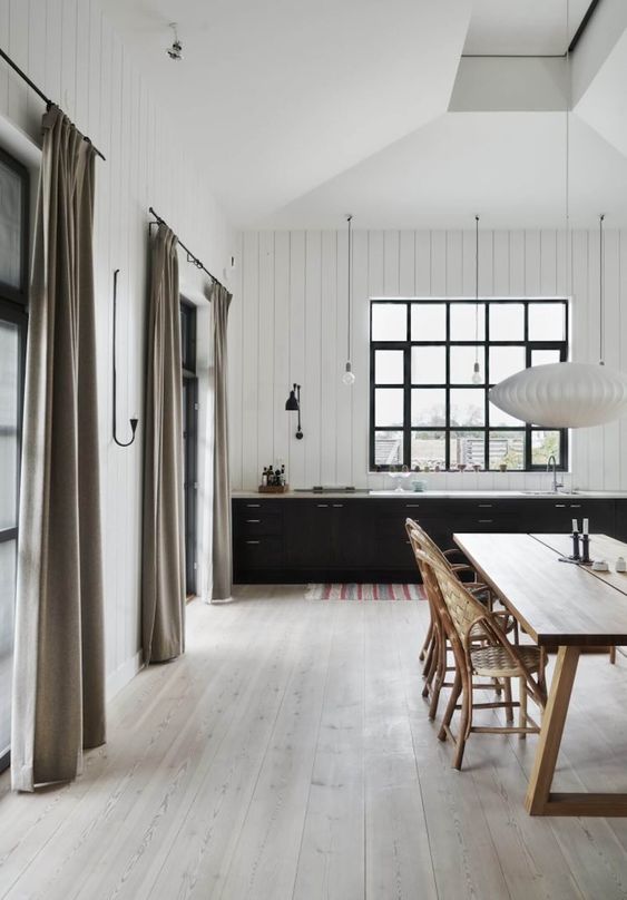 a contrasting kitchen with white walls, black cabinets, whitewashed floors and a lovely wooden dining set