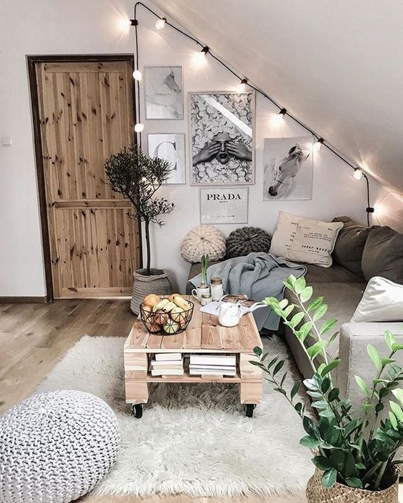 a cozy boho attic living room with a sectional, a pallet table, layered rugs, a gallery wall, string lights and a crochet ottoman