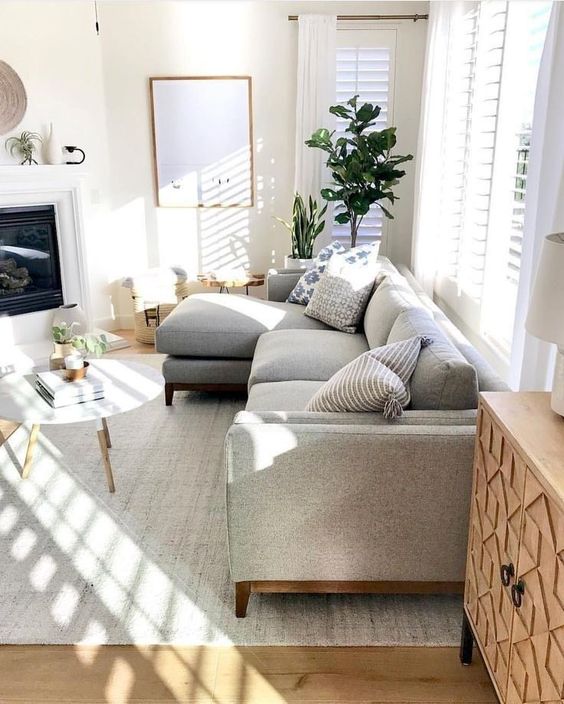 A cozy modern living room with a grey sofa, a built in fireplace, a round table, potted plants and lots of natural light