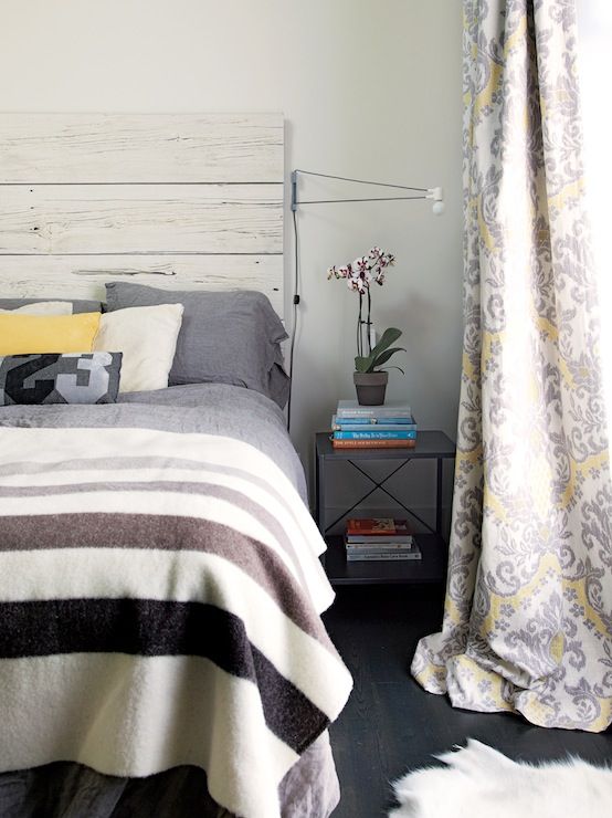 a farmhouse bedroom with a bed with a whitewashed headboard, printed bedding, black nightstands and potted plants is very welcoming