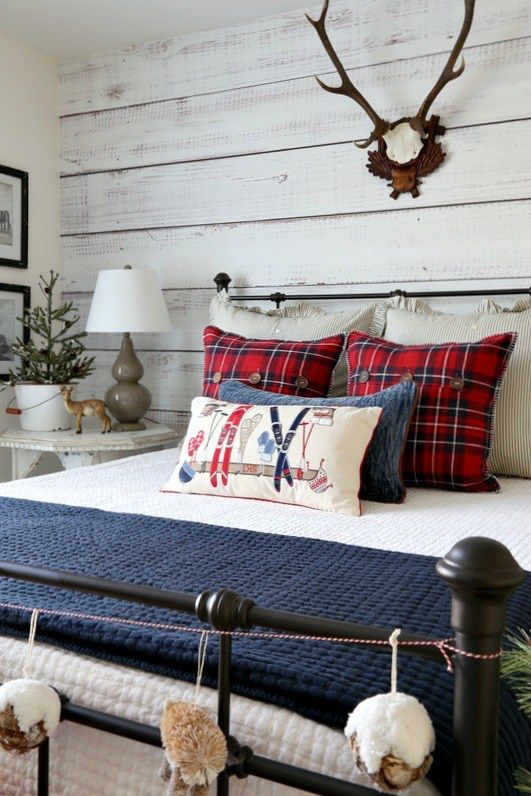 a farmhouse bedroom with a whitewashed wooden wall, a metal bed, whitewashed furniture, bright bedding and antlers on the wall