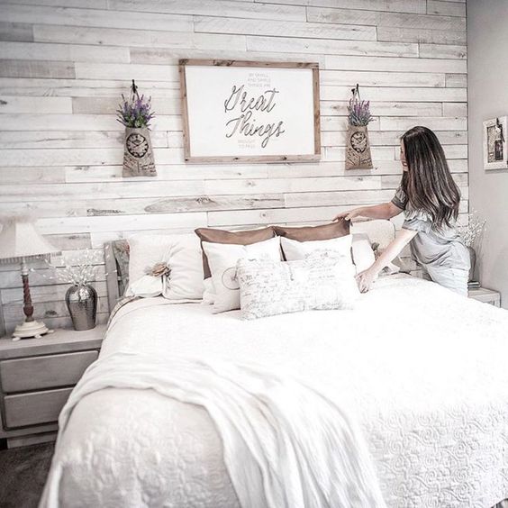 a farmhouse bedroom with a whitewashed wooden wall for an accent, whitewashed furniture, a cozy bed and pendant lavender over the bed
