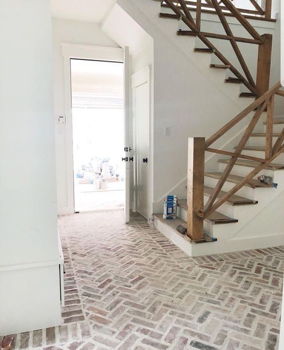 a farmhouse foyer with a whitewashed brick floor and a wooden staircase is lovely and welcoming