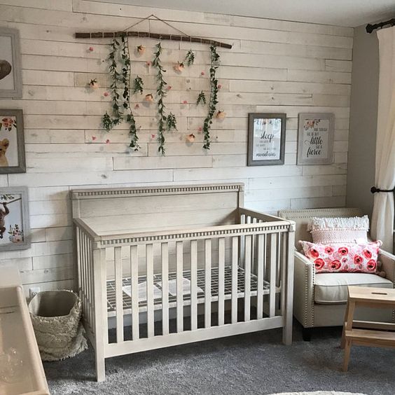 a farmhouse nursery with a whitewashed wooden wall, vintage tan furniture, a floral pendant and artworks is super cool