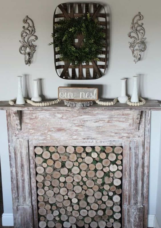 a faux shabby whitewashed wooden fireplace with wood slices in it and some rustic decor is chic