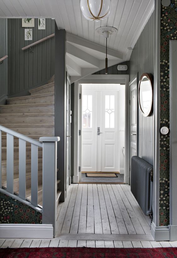 a grey farmhouse entryway with grey walls, a whitewashed floor, a wooden staircase and doors painted white