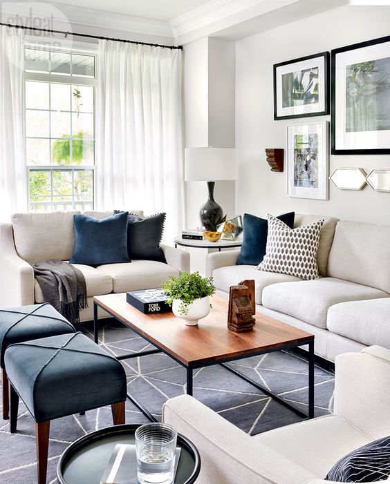 a lively living room with white furniture, navy stools, a wooden table, a printed rug, printed pillows and airy curtains