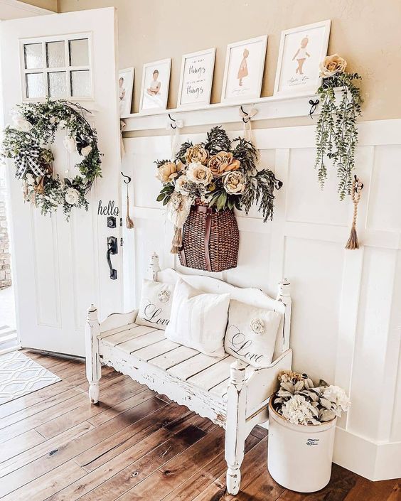 a lovely farmhouse entryway with white paneling, a whitewashed and distressed bench, faux bloom and greenery decor and a pretty vintage gallery wall