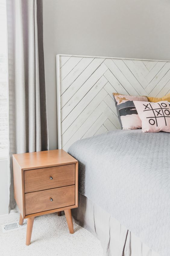 a modern bedroom with grey walls, a bed with a whitewashed herringbone headboard, stained nightstands and printed pillows is super cool