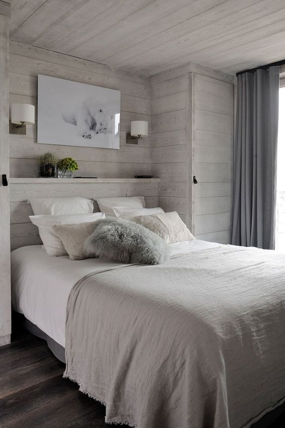 a modern bedroom with whitewashed wooden walls, sconces, an artwork and neutral layered bedding is very cozy