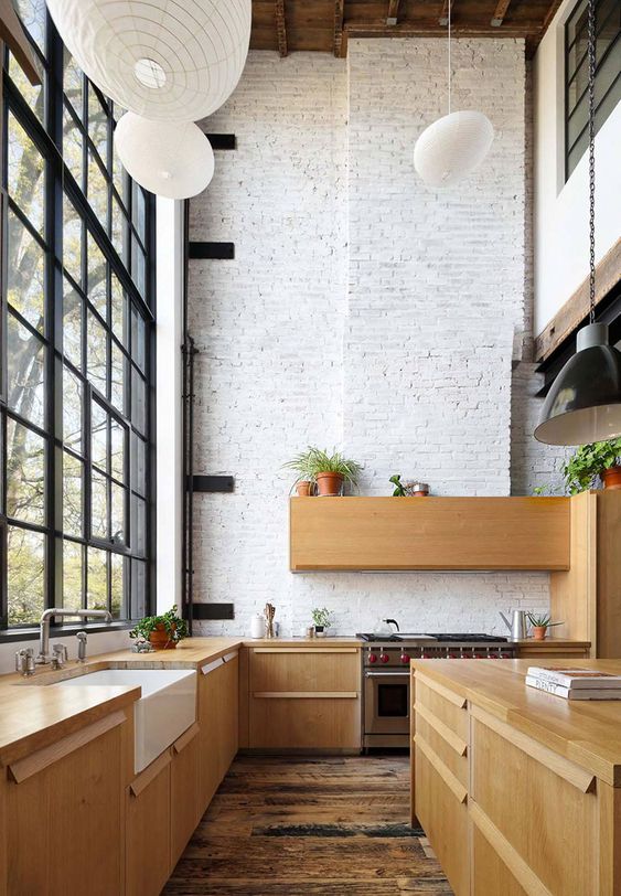 a modern double-height kitchen with whitewashed brick walls, sleek wooden cabinetry, pendant lamps and potted greenery