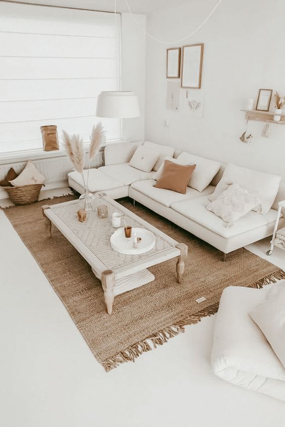 a neutral boho living room with a white sectional, a woven table, a jute rug, pampas grass, a gallery wall and lots of pillows