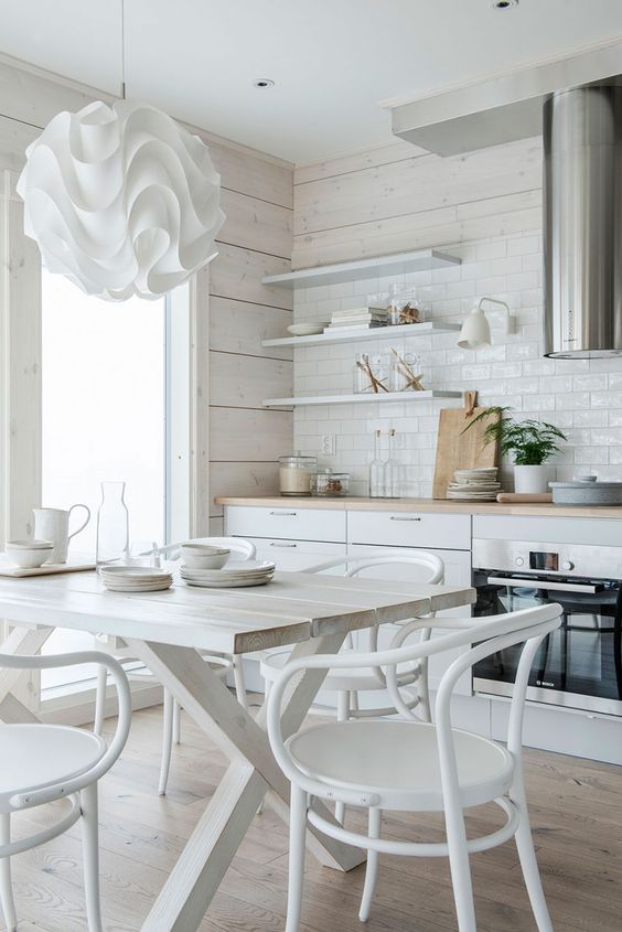 a neutral eat-in kitchen is made catchier with a whitewashed wooden wall, a white tile backsplash and a white dining set plus a ruffle lamp