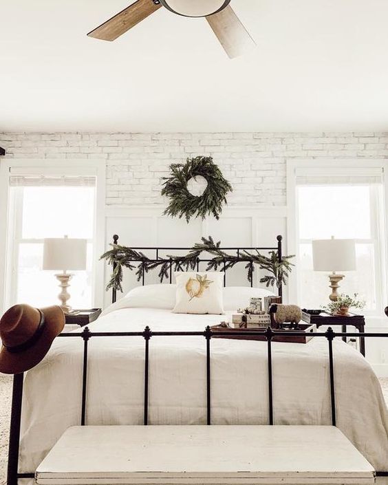 a neutral farmhouse bedroom with whitewashed brick walls, a forged bed, dark nightstands and neutral bedding