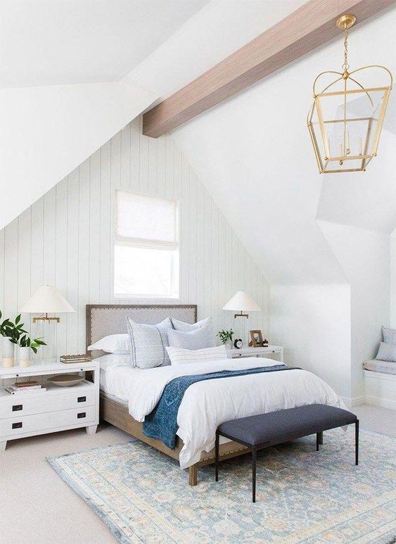 a neutral farmhouse bedroom with whitewashed wooden walls, chic furniture, a wooden beam, a vintage lamp on it and blue bedding