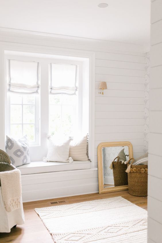 a neutral farmhouse entryway with whitewashed wooden walls, a daybed on the windowsill and pillows and baskets