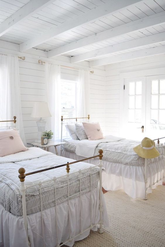 a neutral farmhouse guest bedroom with whitewashed wooden walls and a ceiling, refined vintage beds and a stool with a table lamp