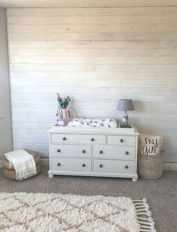 a neutral farmhouse nursery doe with whitewashed wooden walls, a printed linens, a basket with various stuff is a cool space