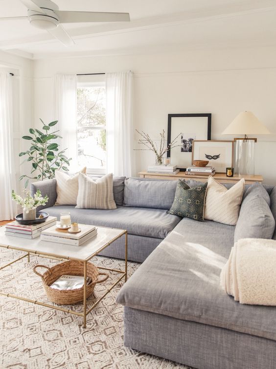 a peaceful small living room with a grey sectional, printed pillows, some plants, a gold table and printed rugs