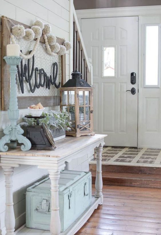 a pretty farmhouse entryway with a whitewashed vintage console table, a blue chest for storage, a candle lantern, a blue candleholder and some beautiful decor