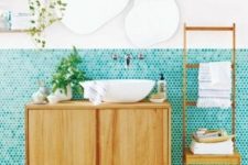 a quirky modern bathroom with turquoise penny tiles, wooden furniture, uniquely shaped mirrors, open shelving and a pendant lamp
