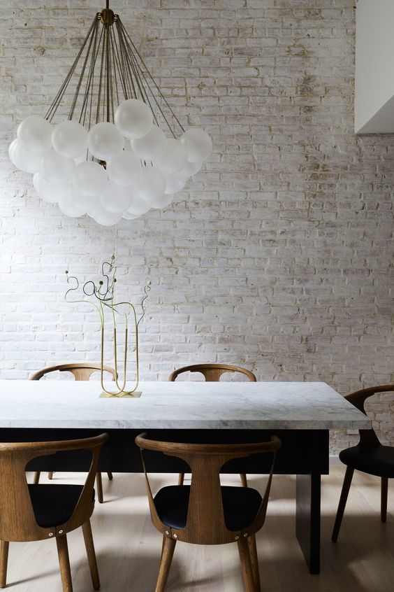 a refined modern dining room with a whitewashed brick walls, a marble table, modern chairs and a cluster of bulbs