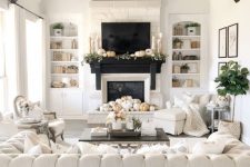 a refined neutral living room with a fireplace, a large and sophisticated tufted sofa, a chandelier, dark beams and white chairs