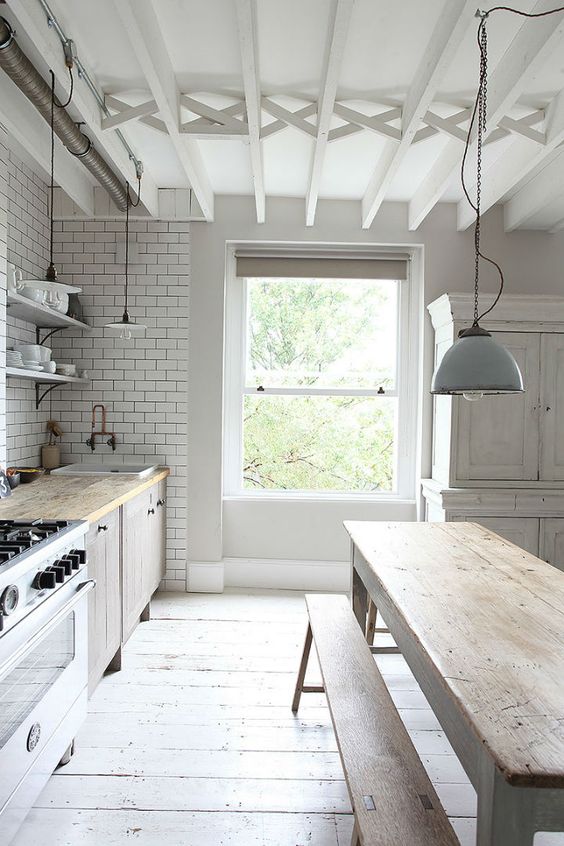 a relaxed Nordic kitchen with white subway tiles, a whitewashed wooden floor and wooden furniture plus pendant lamps