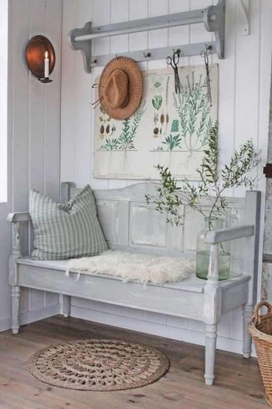 a rustic vintage entryway with a whitewashed bench and a shelf, with botanical posters, candles, a basket and a hat is a lovely space