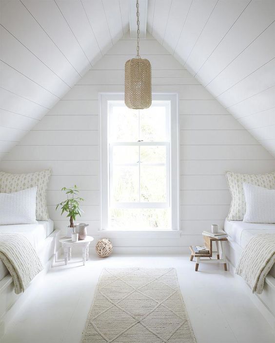 a serene attic guest bedroom with whitewashed wooden walls and white beds, a pendant lamp and neutral printed bedding