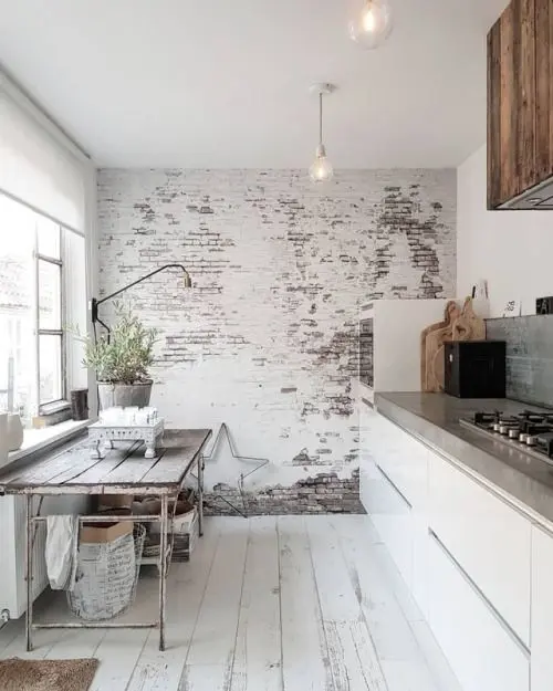 a shabby chic Nordic kitchen with a whitewashed brick wall, sleek white cabinetry, a vintage table and potted plants