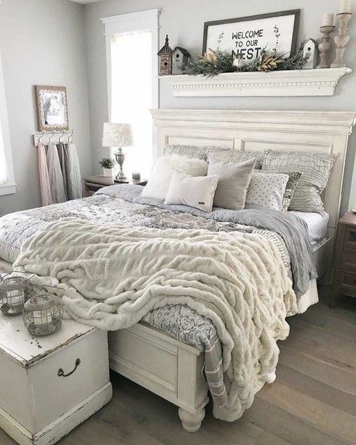 a shabby chic bedroom with grey walls, a whitewashed bed and stained nightstands, table lamps and candles, artwork and candle lanterns