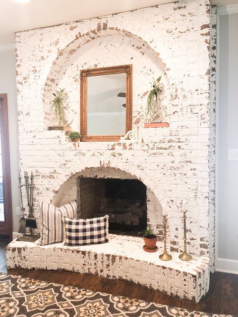 a shabby chic whitewashed fireplace with a mirror, potted greenery, printed pillows and candles in candlesticks