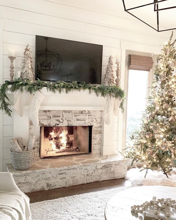 a shabby whitewashed fireplace with a mantel decorated for Christmas and a basket with firewood