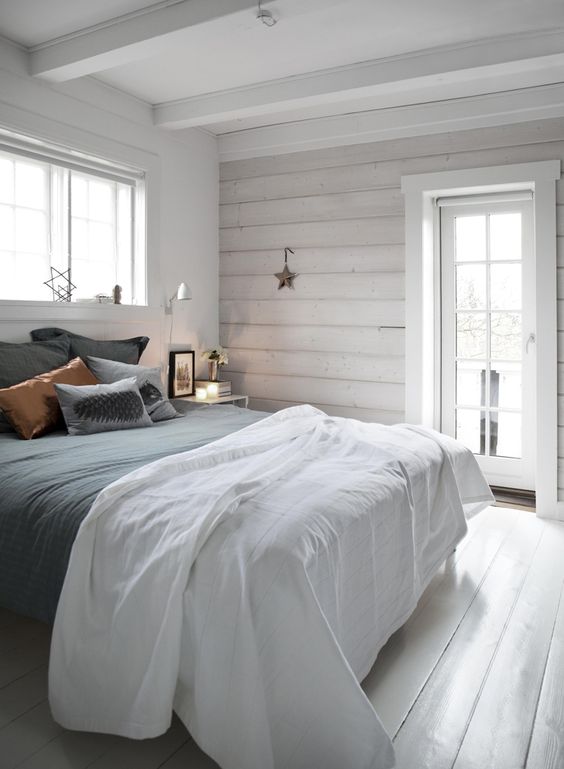 a simple Nordic bedroom with whitewashed wooden walls, a bed with grey and copper bedding, stars and sconces is welcoming