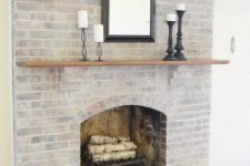 a simple and stylish whitewashed brick fireplace with firewood, a mantel, candles and a mirror for adding coziness to your space