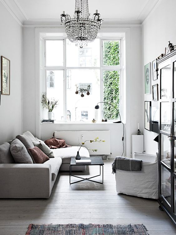 a small Scandinavian living room in a neutral color palette, with comfy and simple furniture, a crystal chandelier and a gallery wall