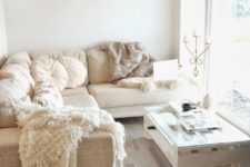 a small and neutral glam living room with a sectional sofa, a pallet table, a fur rug, a lamp with crystals