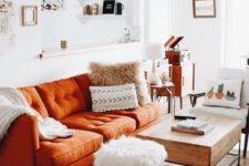 a small boho living room with a rust-colored sofa, printed pillows, a wooden table, mid-century modern furniture and a boho rug