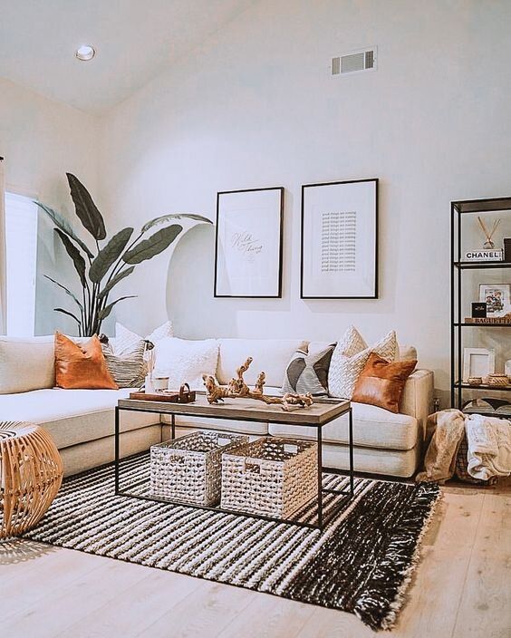 a small boho living room with a white sectional, woven and wooden items, a gallery wall, potted plants and printed pillows