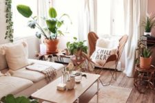 a small boho living room with a white sofa, a leather butterfly chair, a wooden table and lots of plants on stands