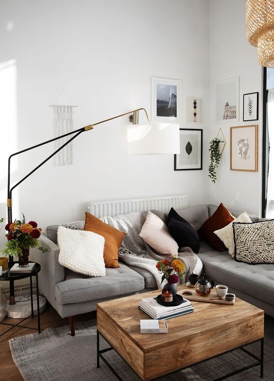 a small contemporary meets boho living room with a grey sectional, a wooden table, a gallery wall, a floor lamp and bright pillows