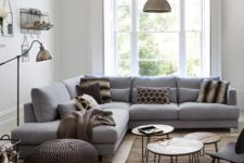 a small cozy living room with a grey sofa, knit ottomans, metal lamps, pin leg tables and a large window